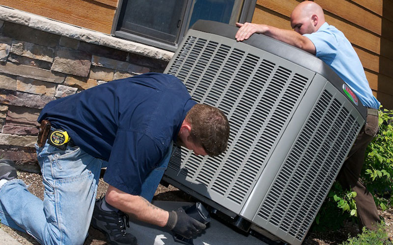 Two men working on an air conditioner in front of a house.