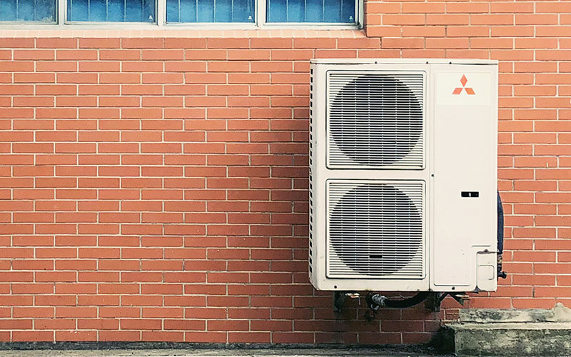 An air conditioner is sitting on a brick wall.
